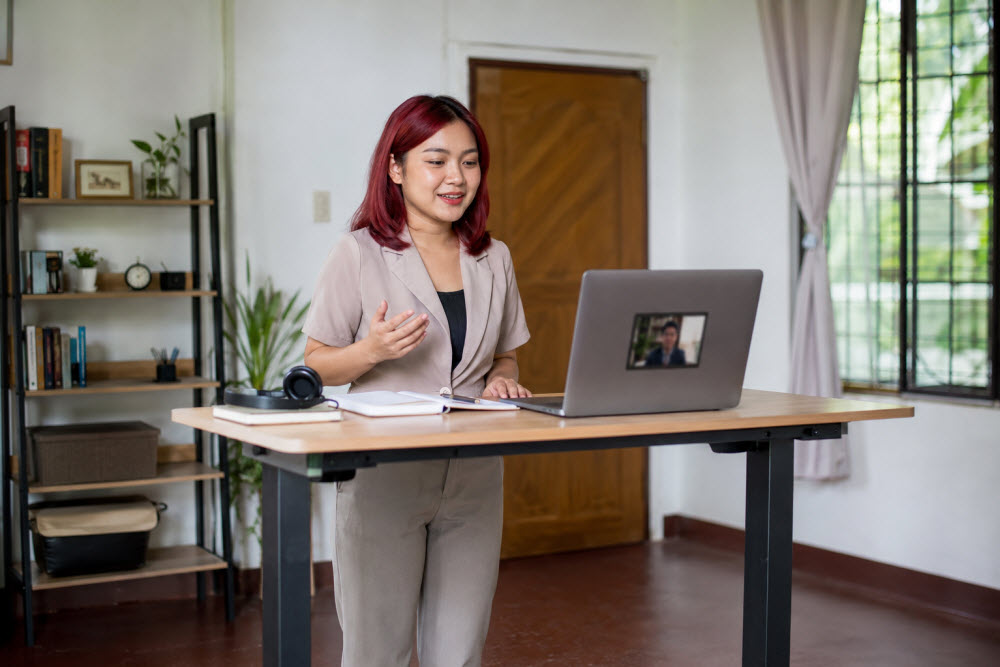 Young Filipina virtual assistant with red hair attending an online interview at a standing desk.